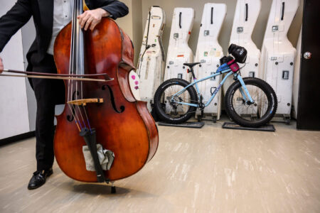 A Winnipeg Symphony Orchestra performer tunes up their instrument as a bicycle is parked in the background amid bass storage containers