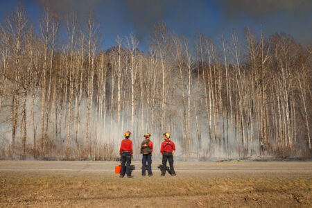 BC Wildfire Service members standing alongside a road with smoke in the forest