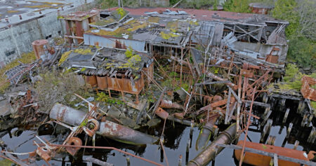 At Namu, in the Great Bear Rainforest, a heap of rusted metal pipes, walls and bars are in disarray, some half submerged in ocean water, and buildings are grown over with grass