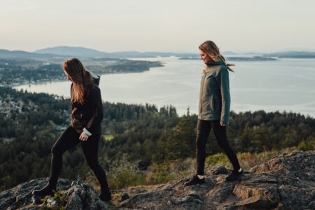 The Narwhal's co-founders Carol Linnitt (left) and Emma Gilchrist (right) walking on a rocky hill, with the ocean in the background.