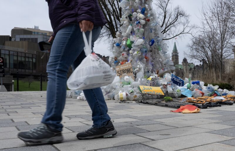 A person carries food in a plastic bag past a plastic public art installation outside the a United Nations conference on plastics on Tuesday, April 23, 2024 in Ottawa