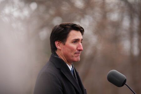 Prime Minister Justin Trudea in a black coat outside at a microphone looking forlorn