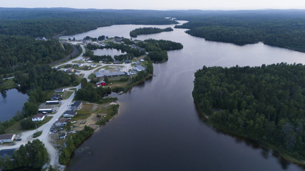 Netmizaaggamig Nishnaabeg: An aerial view of a lake with a few houses along a gravel road tucked next to it