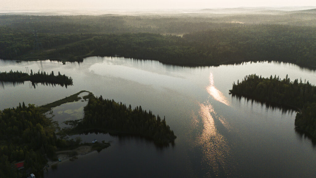 Ontario mining boom: Sunlight reflects off of the water of a lake as mist rises from a forest behind it