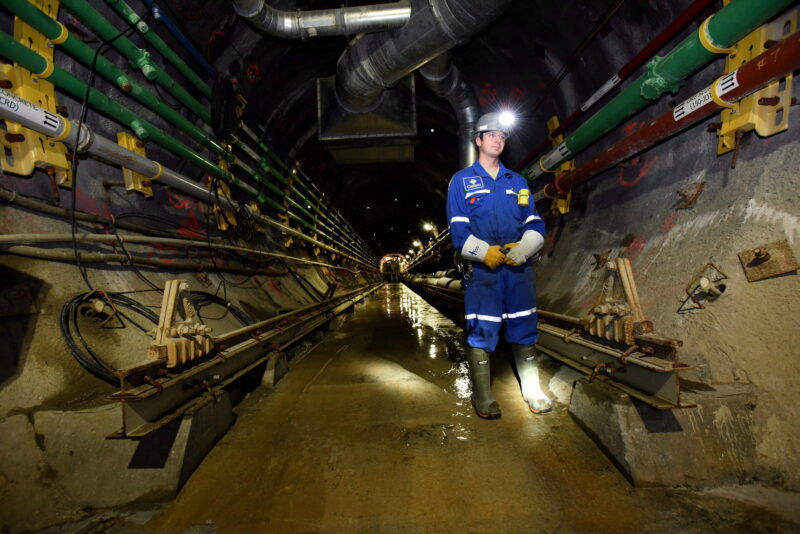A miner in blue coveralls stands in a uranium mine corridor underground.