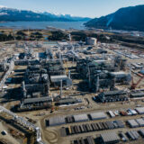 An aerial view of the LNG Canada project site, looking toward the water with snow capped mountains in the background
