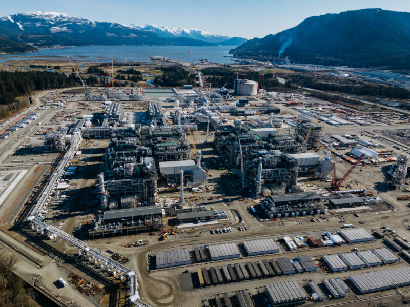 An aerial view of the LNG Canada project site, looking toward the water with snow capped mountains in the background