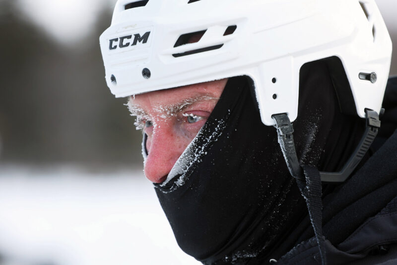 Close up of a frost-covered pond hockey player wearing a helmet and balaclava with ice forming on his eyelids and eyebrows