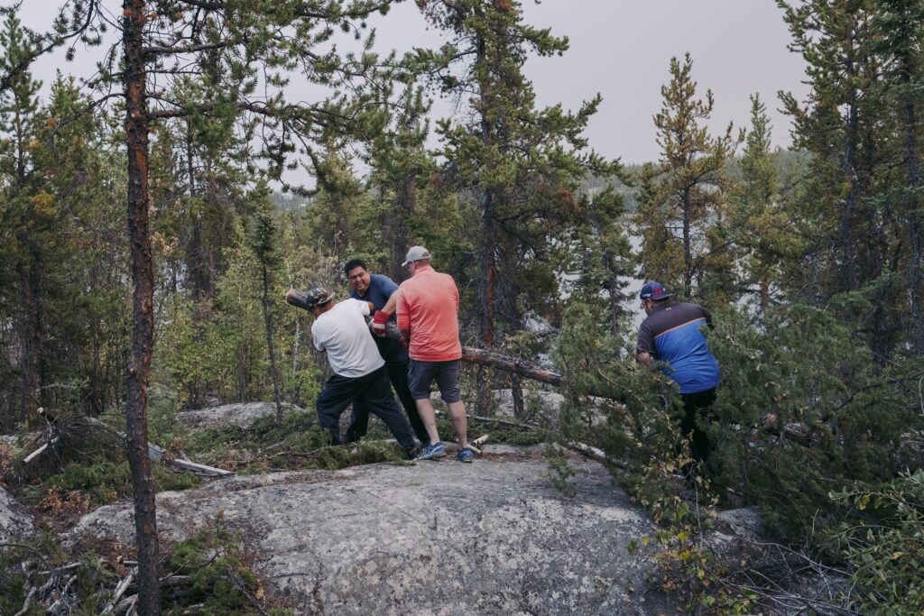 Four men work together to drag a felled tree across rocky ground