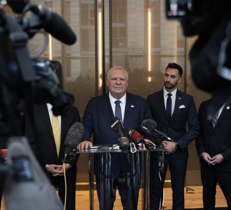 Ontario Premier Doug Ford stands at a podium in front of cameras with Energy Minister Stephen Lecce behind him