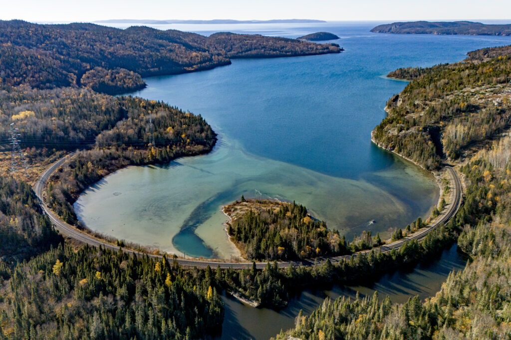 Aerial view of Jackfish Bay on Lake Superior with a railway wrapping around the shore bend and silty water flowing into turquoise