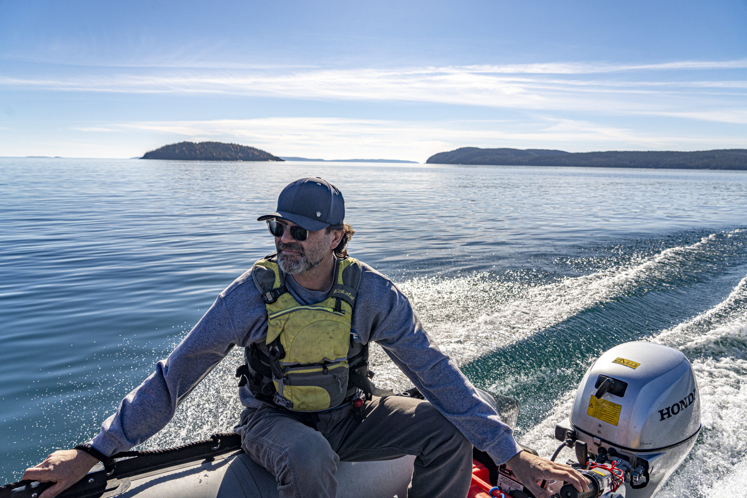 A man wearing a life jacket drives a zodiac boat on Lake Superior with islands in the background