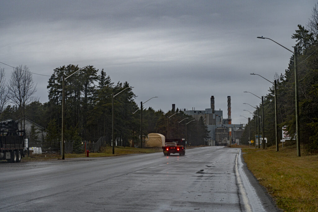 A car drives down a wet roadway towards the shuttered pulp mill in Terrace Bay, Ont., under grey skies