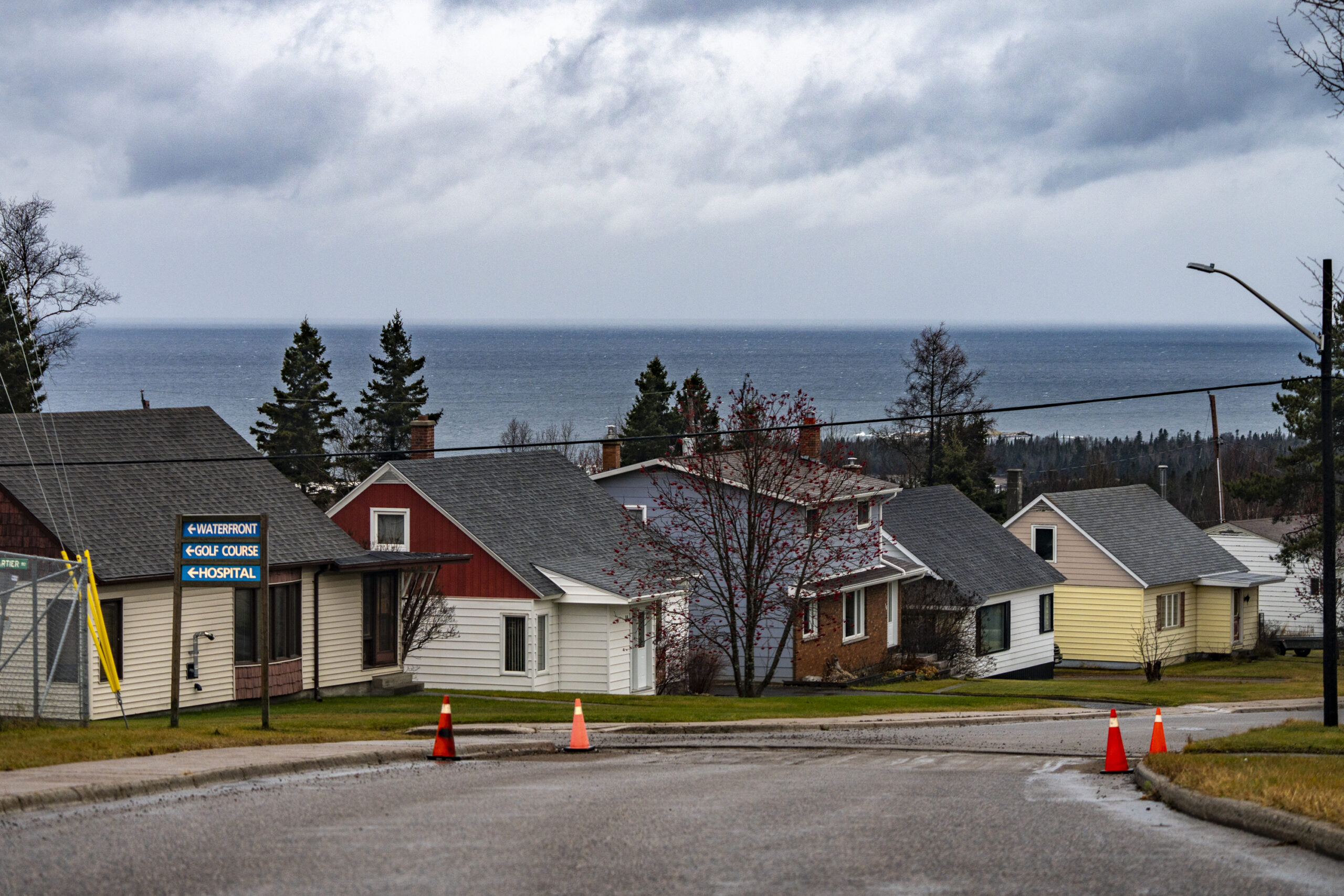 Houses line a street in Terrace Bay, at the shore of Lake Superior, with pilons on the road marking off potholes