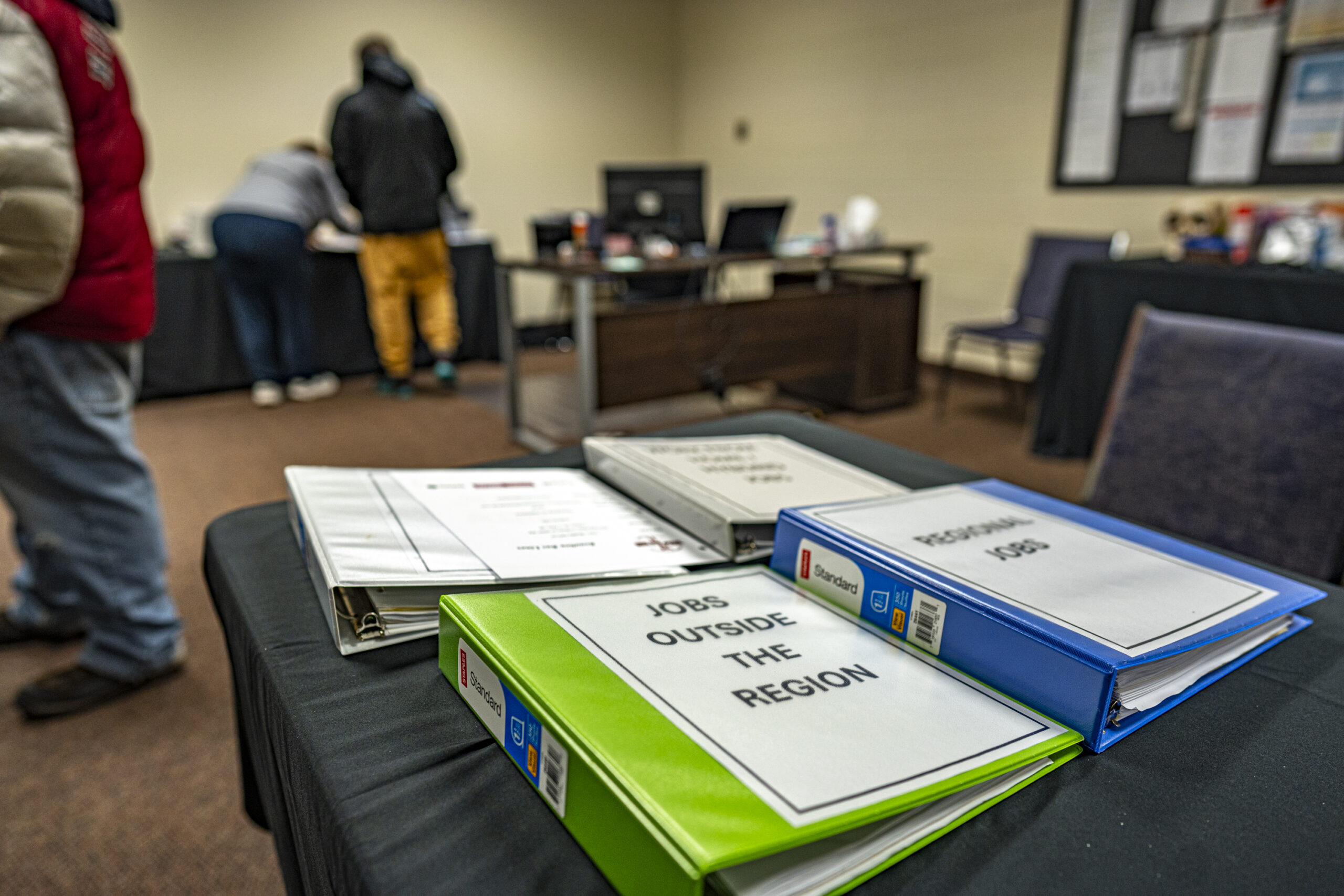 Binders that read 'jobs outside the region' and 'regional jobs' sit on a table with people in the backgroun
