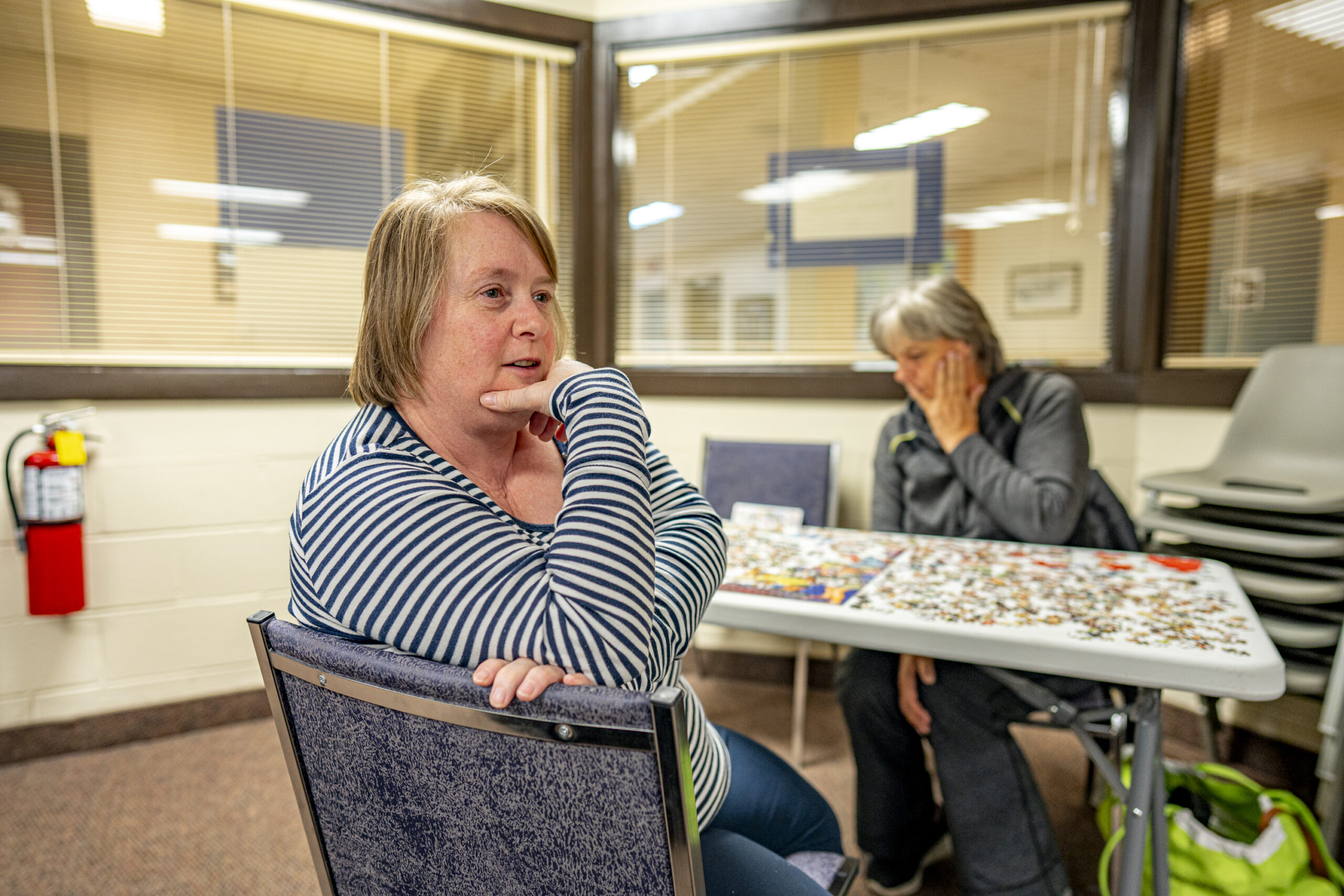 A woman looks back from a table where another woman sits working on a puzzle in an office