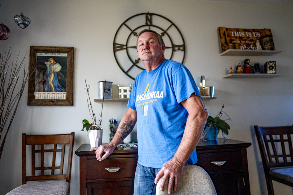 A man in a blue t-shirt stands in his home in front of a wall-mounted compass rose