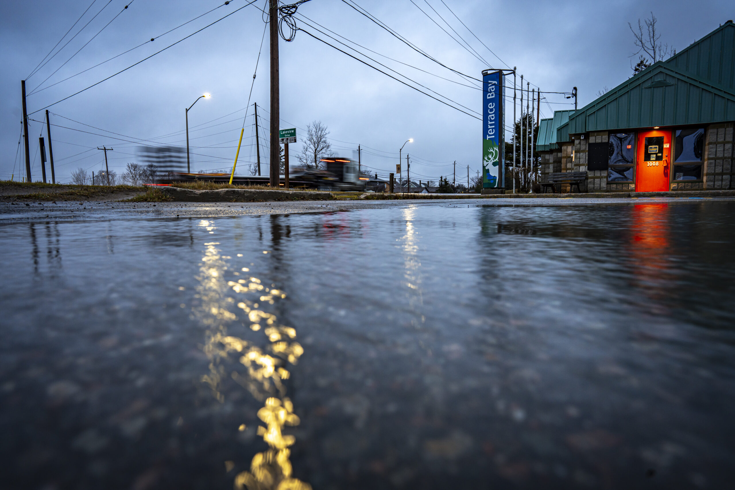 Water pools on the ground under cloudy grey skies outside a building with a sign for "Terrace Bay"