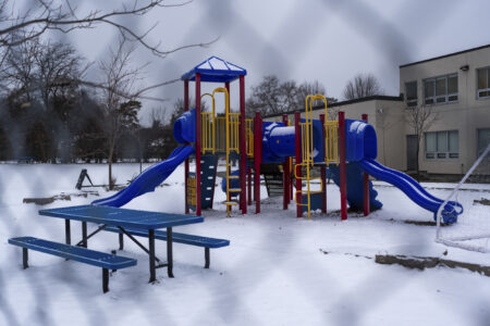 A play structure is surrounded by fresh snow, pictured through blurry chain link fence