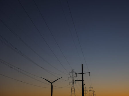 Power lines and a wind turbine silhouetted against a bigdusk sky
