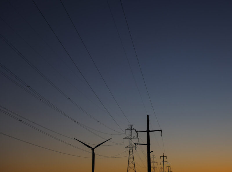 Power lines and a wind turbine silhouetted against a bigdusk sky