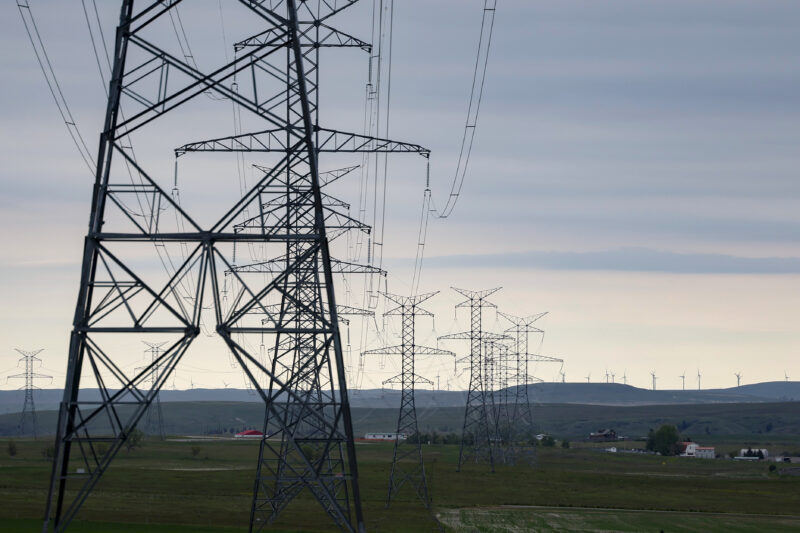 Transmission towers stretch off into the distance, connected by wires with wind turbines on a far-off ridge.