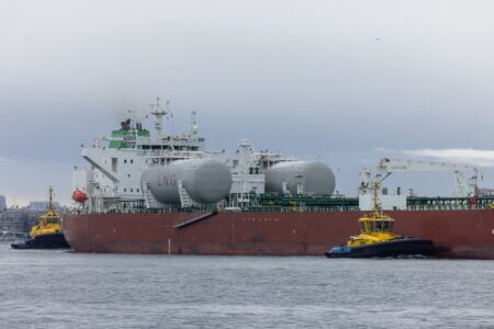 A large ship is pulled by two tugboats. The ship has two enormous tanks with "LNG" painted on them