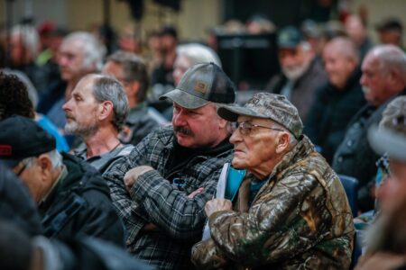 Men in camo and baseball caps watch a presentation at an information session for Indigenous led protected areas