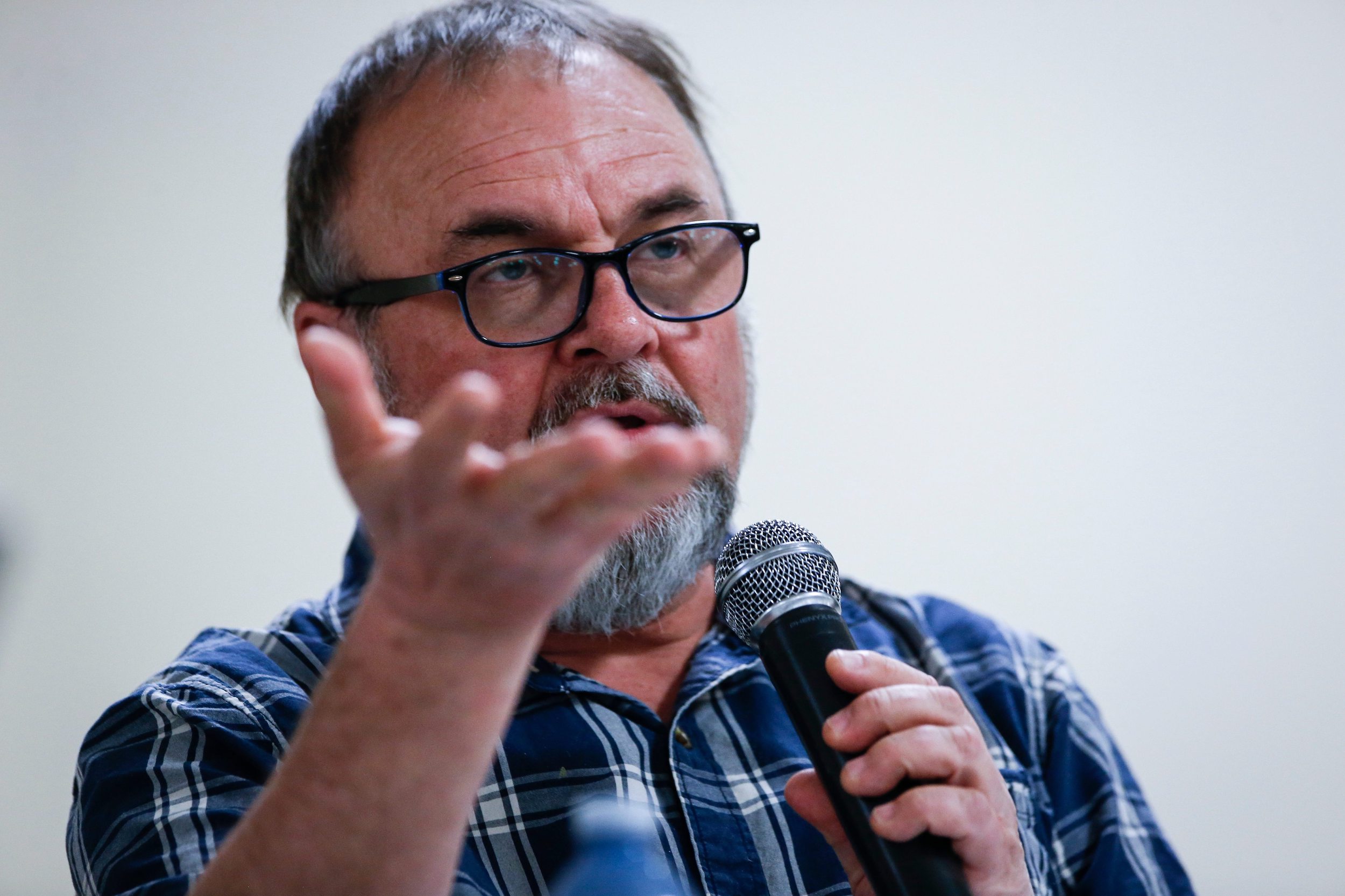 A close-up of a man in glasses speaks at a microphone