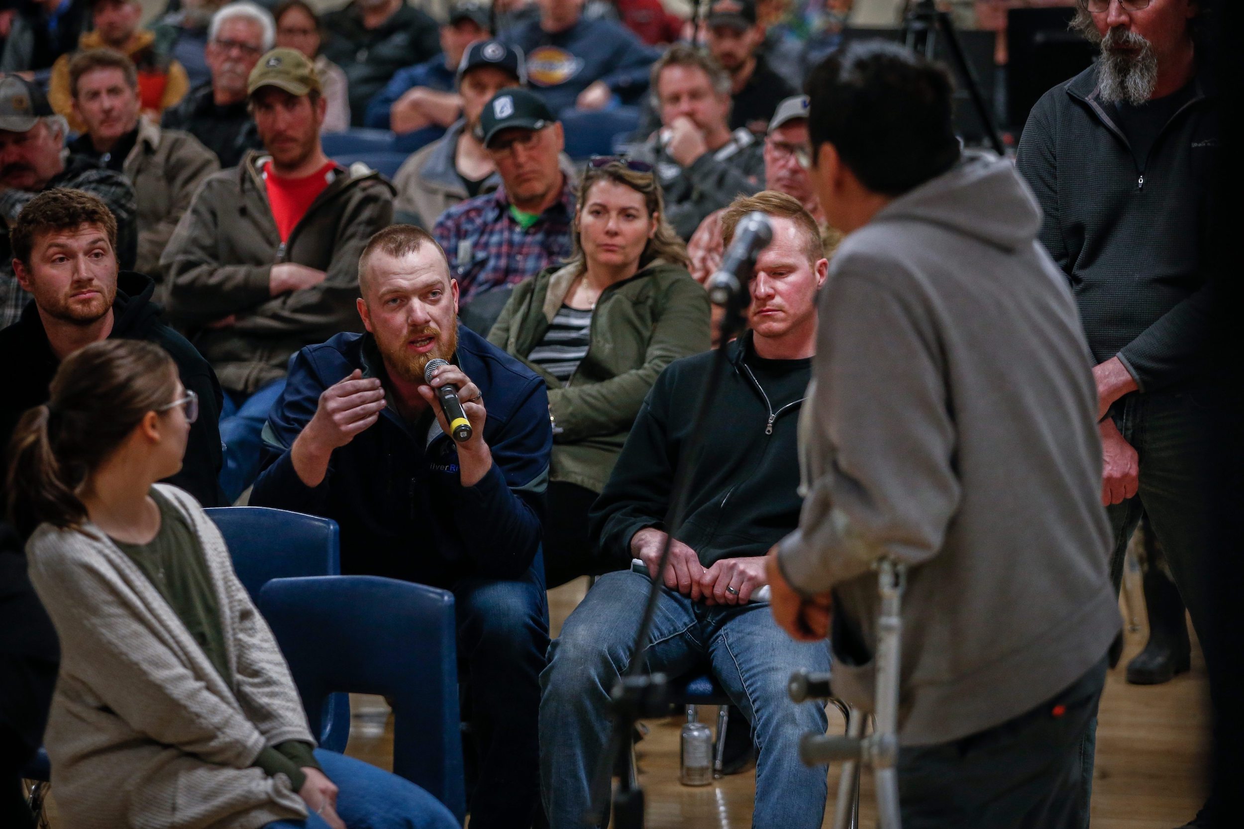 Two people with microphones speak to each other in front of a large crowd