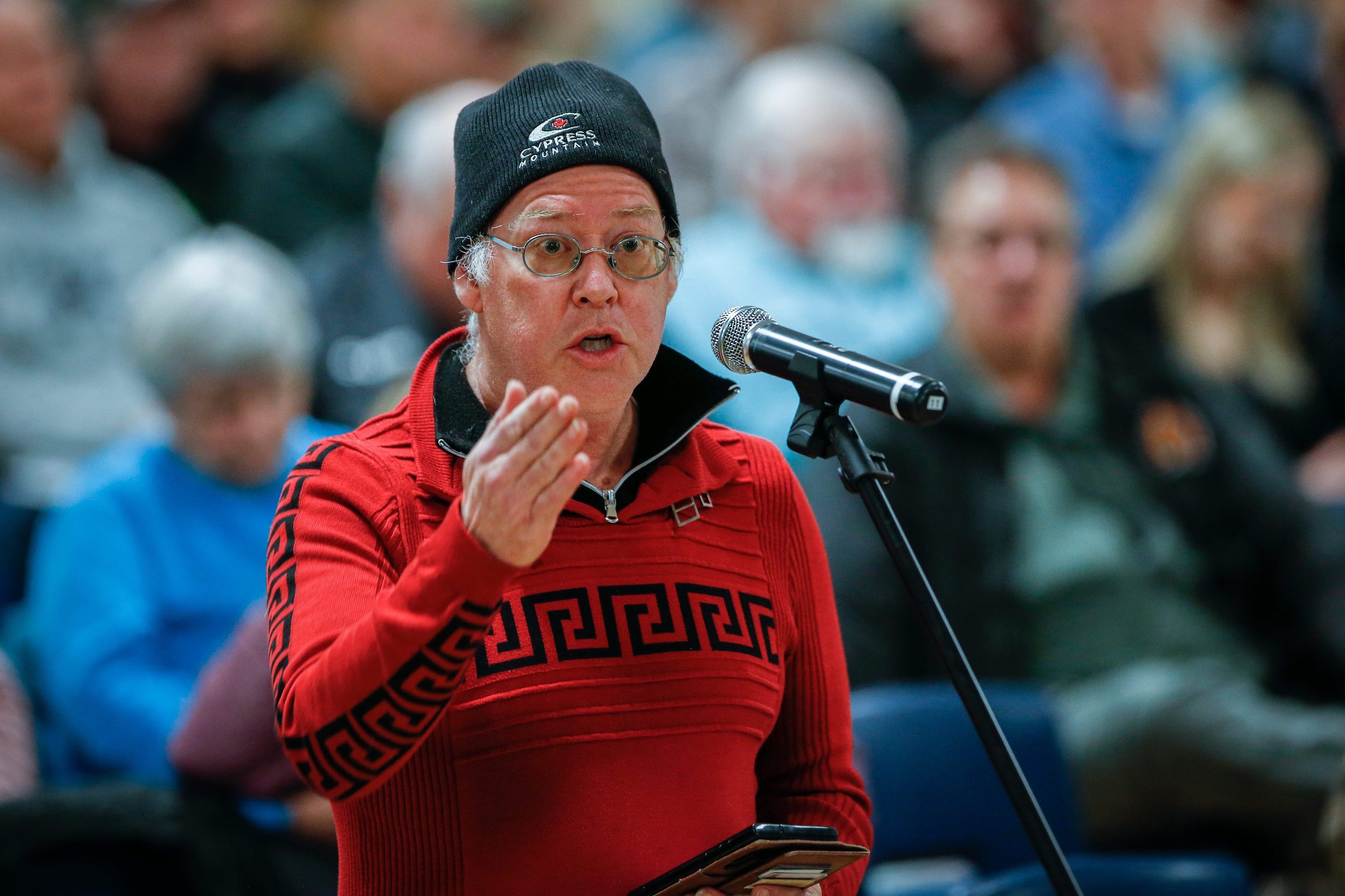 A man in a red shirt and a black toque speaks at a microphone