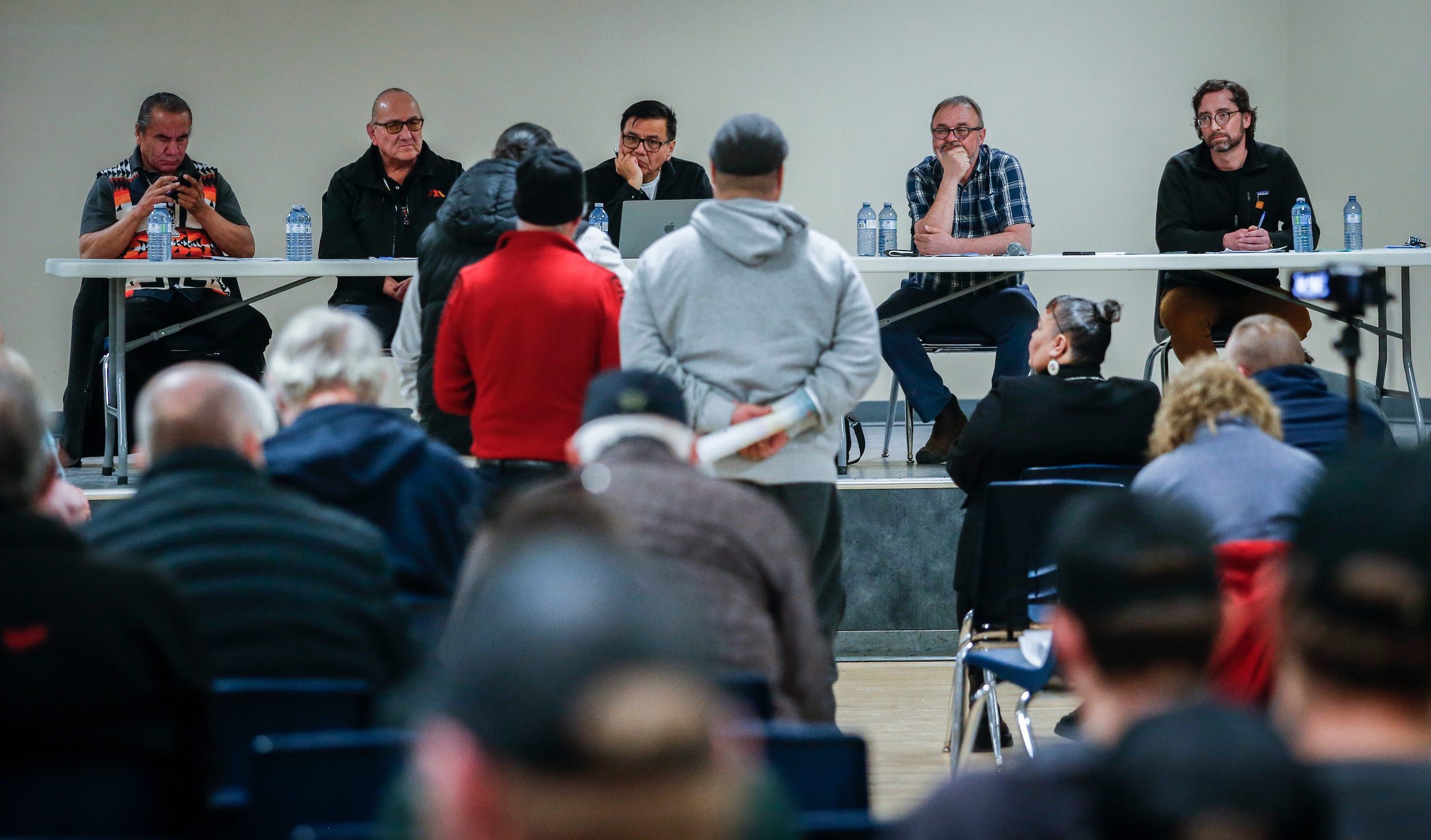 People line up at a microphone to speak to a panel in front of a large crowd