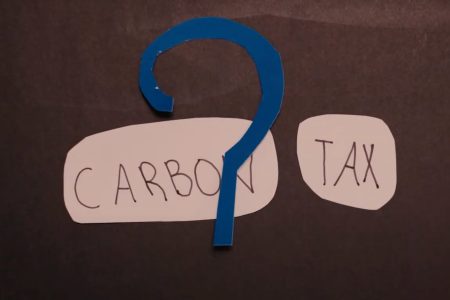 The words carbon and tax are handwritten on scraps of paper. A paper cut out of a question mark is laid over them.
