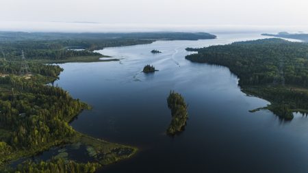 An aerial view of a motorboat on White Lake in Netmizaaggamig Nishnaabeg territory in northern Ontario, with thick forest on the shoreline