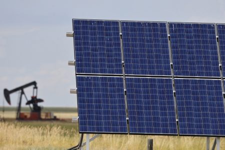 A solar panel in a field in Alberta, with an old pumpjack in the distance.