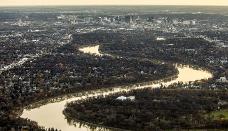 Aerial view of Winnipeg's skyline with the river winding through the centre of frame and reflecting the yellow glow of the sun
