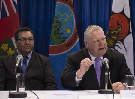 Two men sitting at a table in front of microphones, one speaking and gesturing