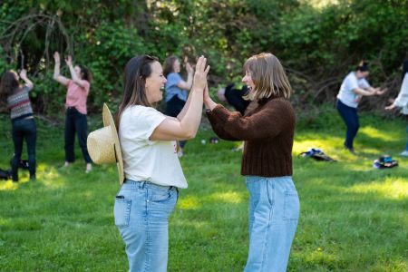 Two people double-high-five each other and laugh. They are in a large circle of people doing the same thing