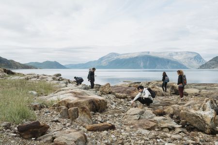 A group of five people, students and visitors, explore a rocky beach on an island in Torgngat Mountains National Park