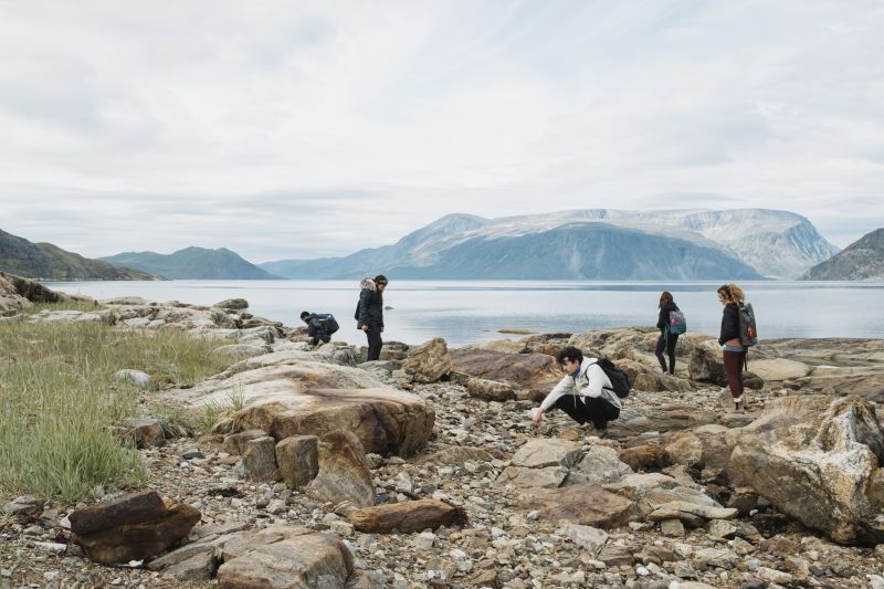 A group of five people, students and visitors, explore a rocky beach on an island in Torgngat Mountains National Park