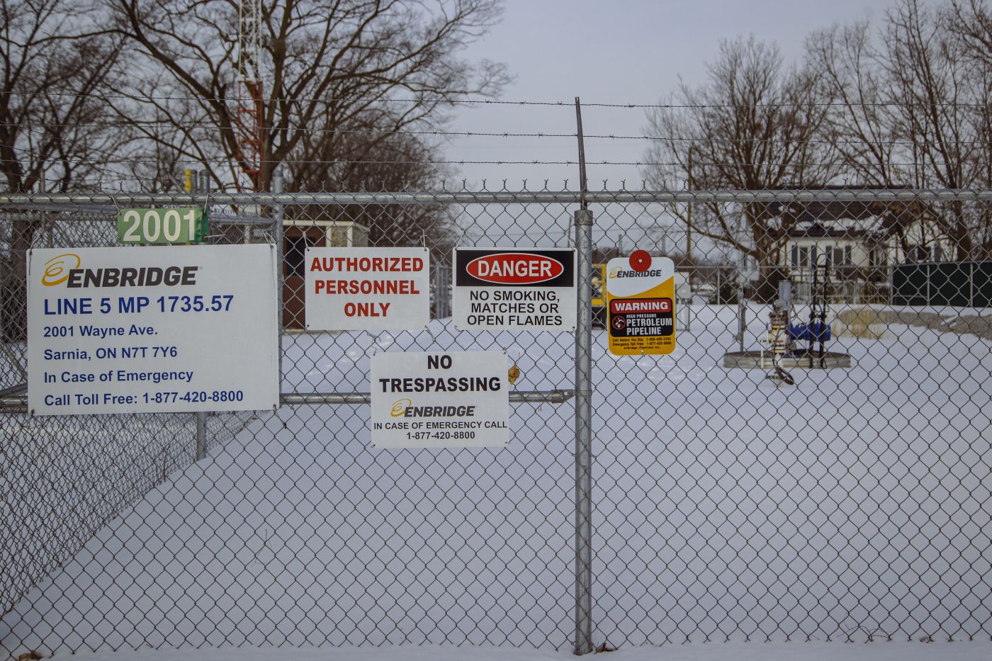 A fence with various warning signs about trespassing, danger and pipelines on it