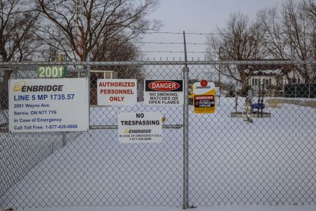 A fence with various warning signs about trespassing, danger and pipelines on it
