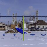 A blue and green swingset in front of a small building, with smokestacks in the background