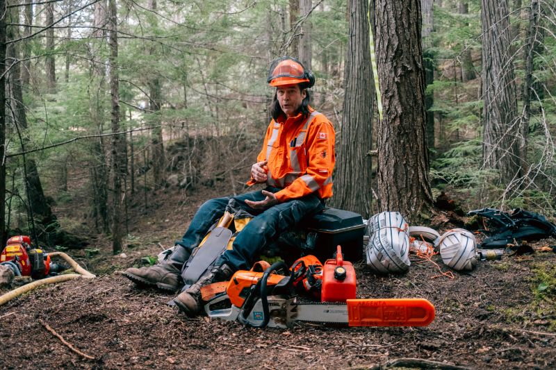 A volunteer firefighter sits beside a chainsaw and gas during a fire training in Argenta, B.C.