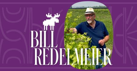 A photo of winery owner Bill Redelmeier wearing a fedora and standing in the vineyard.