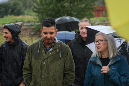 A photo of a group of people walking with umbrellas in the rain with trees in the background