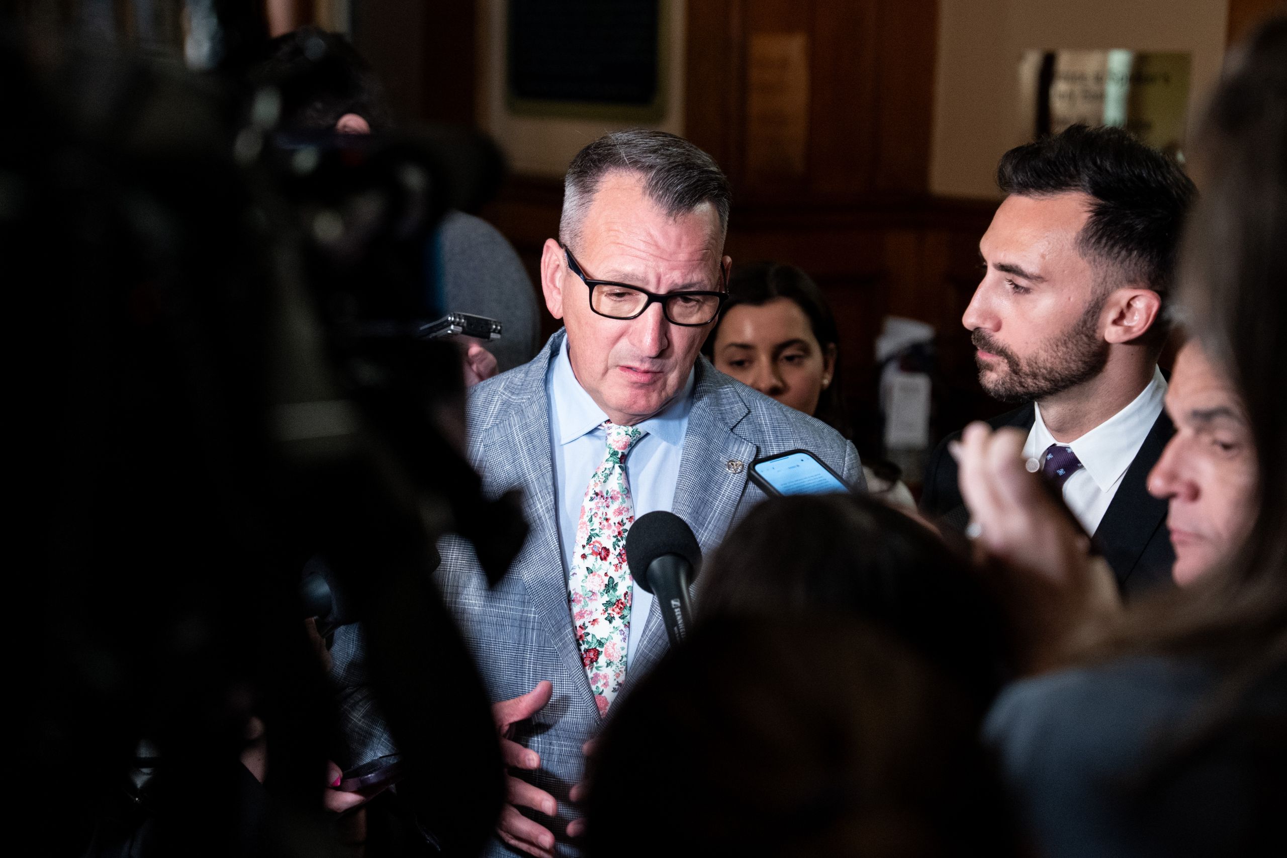 Two men in suits are seen speaking to reporters inside the Ontario legislature.