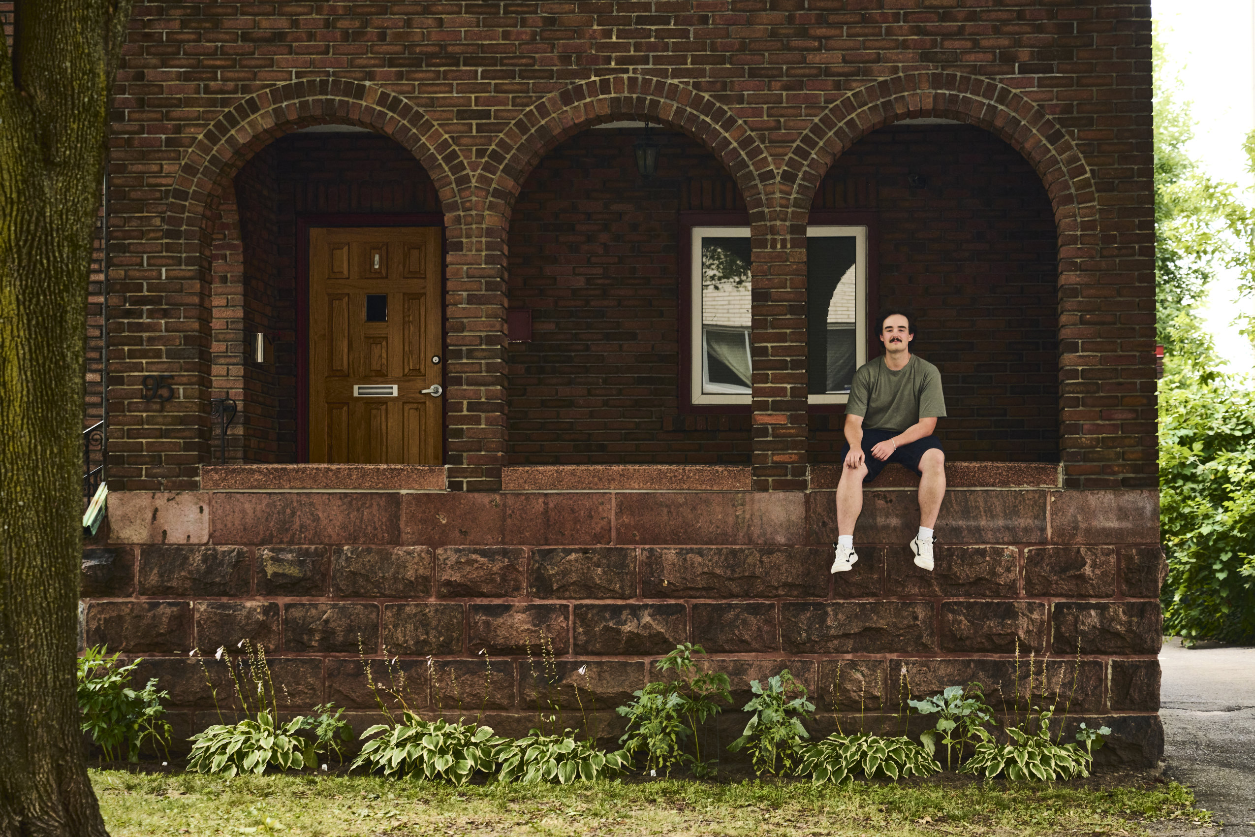 A young man sits atop a low wall, framed by one of three brick arches.