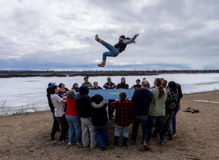 About 20 people hold a large circle of fabric, using it like a trampoline to launch a person high into the air