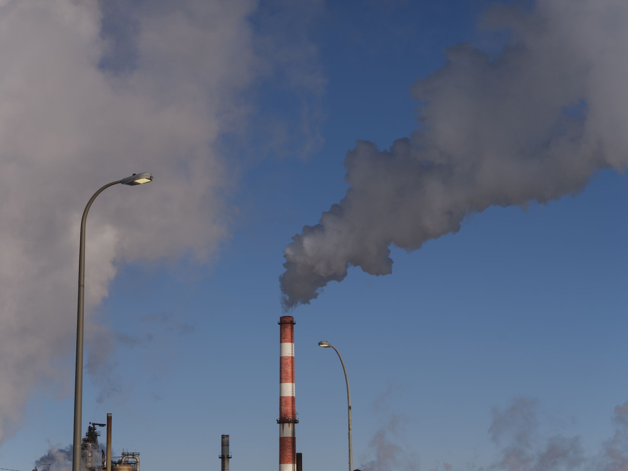 A red-and-white smokestack expels clouds of smoke against a blue sky.